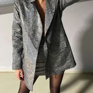 Bir kadın otoparkta parlak ceket ve altında parlak eteğiyle poz veriyor