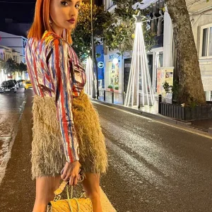 yakası açık parlak kumaş saçak detaylı etek ile birleşmiş tek parça mini karla elbise ile gece caddede poz veriyor