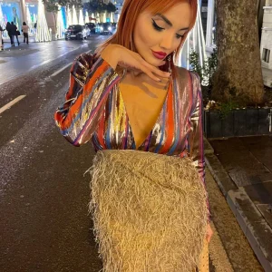 yakası açık parlak kumaş saçak detaylı etek ile birleşmiş tek parça mini karla elbise ile gece caddede poz veriyor